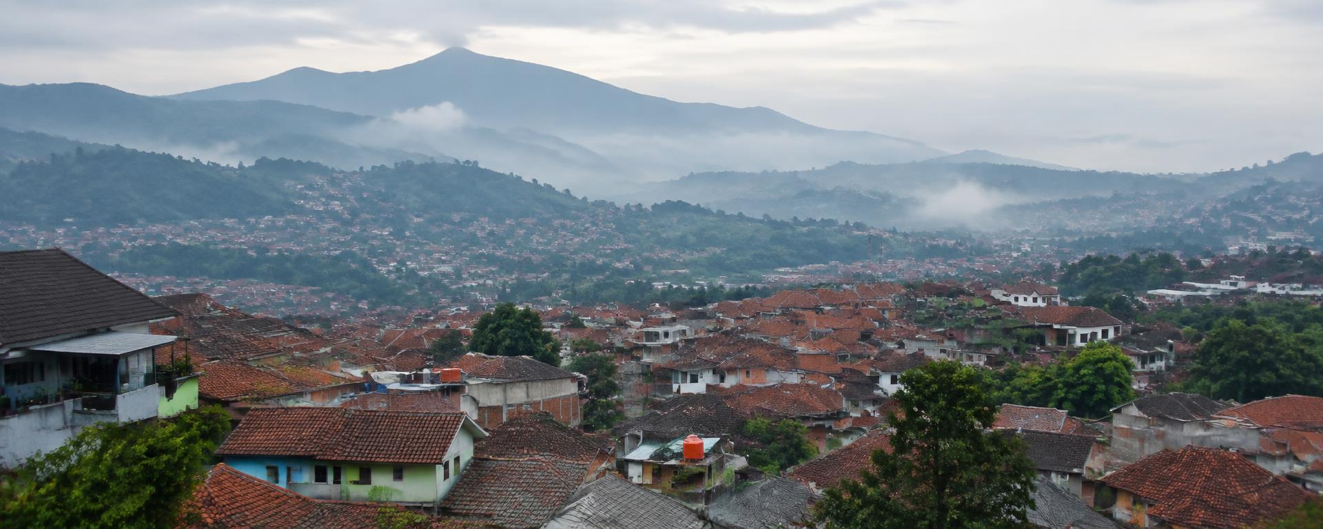 Tiled rooftops of Bandung with misty green hills behind